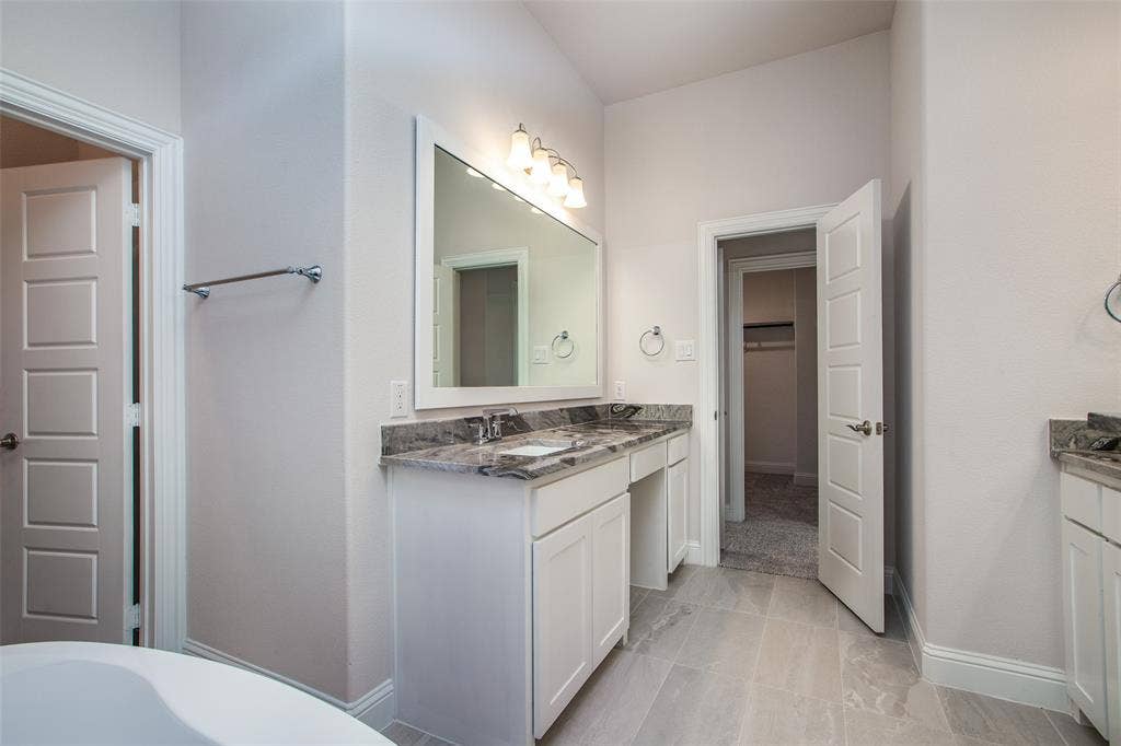 4944 Mckinney Hollow Drive, McKinney, TX 75070 Dual vanity with stone countertops, white cabinetry, and a framed mirror with integrated lighting