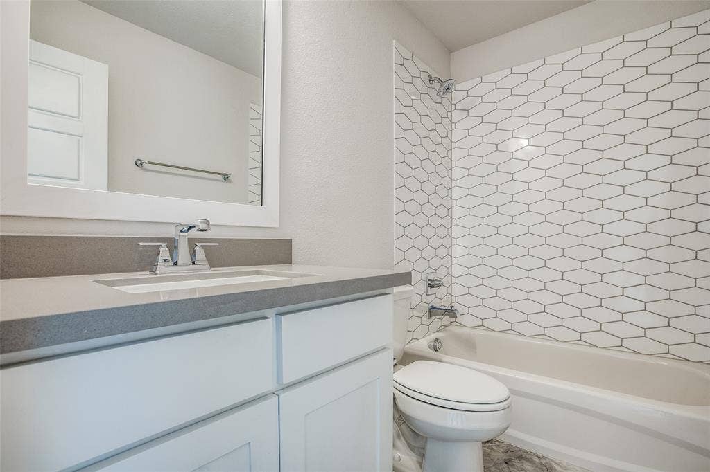 4944 Mckinney Hollow Drive, McKinney, TX 75070 White shaker cabinetry, grey countertop, undermount sink with chrome faucet, hexagon-patterned tub surround, and a white bathtub