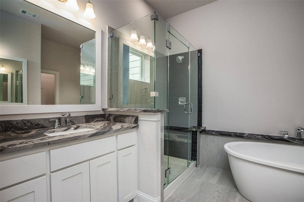 4944 Mckinney Hollow Drive, McKinney, TX 75070 Spacious bathroom featuring a freestanding tub, glass-enclosed shower, dual vanity with undermount sinks, and stone countertops