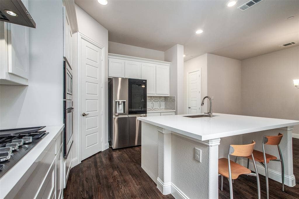 4944 Mckinney Hollow Drive, McKinney, TX 75070 White kitchen cabinetry, stainless steel appliances, solid surface countertops, wood-finish flooring, and recessed lighting
