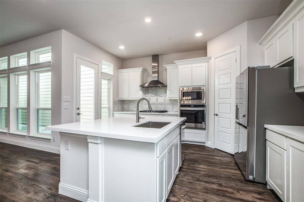 4944 Mckinney Hollow Drive, McKinney, TX 75070 Kitchen featuring a central island with an undermount sink, white cabinetry, stainless steel appliances, and wood-finish flooring