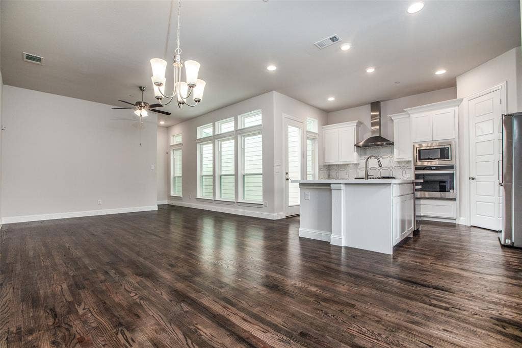 4944 Mckinney Hollow Drive, McKinney, TX 75070 Dark wood-finish flooring throughout, white cabinetry, stainless steel appliances, a kitchen island, and multiple large windows