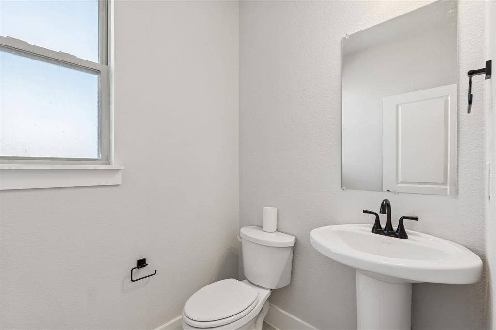 410 Rancher Trail, Waxahachie, TX 75165 Pedestal sink with a matte black faucet, wall-mounted mirror, and a window with white trim