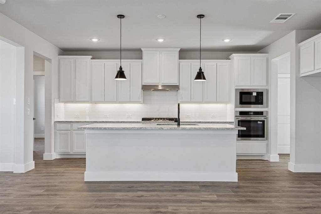 410 Rancher Trail, Waxahachie, TX 75165 Kitchen featuring white cabinetry, a central island with a sink, stainless steel appliances, and wood-finish flooring