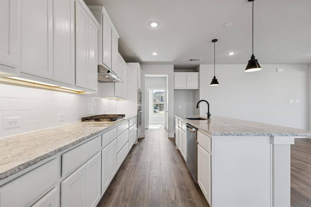410 Rancher Trail, Waxahachie, TX 75165 Galley kitchen featuring white shaker cabinetry, light-toned stone countertops, a full stainless steel appliance package, a built-in cooktop, and wood-finish flooring