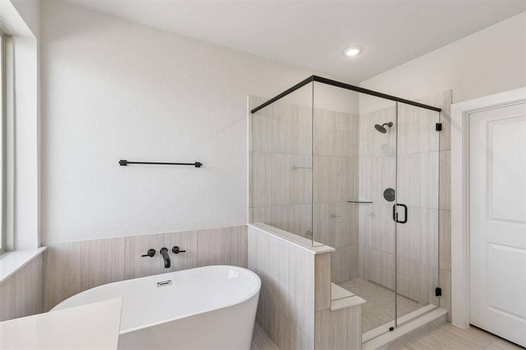 410 Rancher Trail, Waxahachie, TX 75165 Freestanding soaking tub with wall-mounted matte black faucet, glass-enclosed shower with matte black fixtures, and light-toned tile flooring