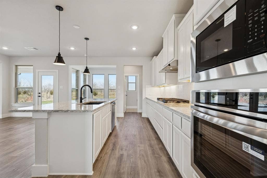 410 Rancher Trail, Waxahachie, TX 75165 White cabinetry, stone countertops, stainless steel appliances, wood-finish flooring, and recessed lighting