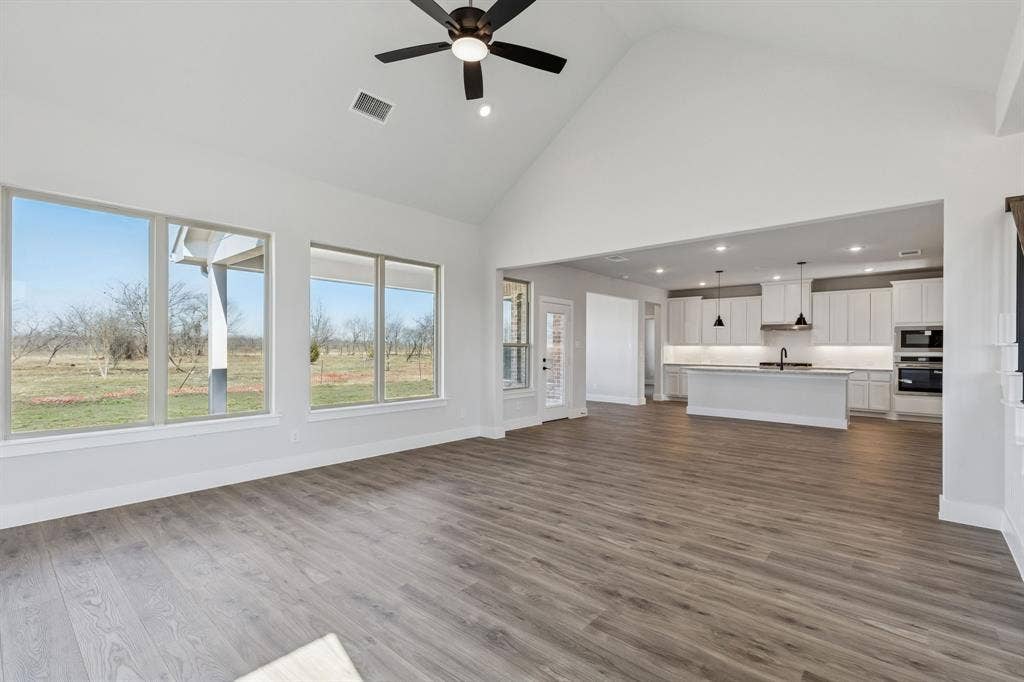 410 Rancher Trail, Waxahachie, TX 75165 Vaulted ceiling with a ceiling fan, wood-finish flooring, ample natural light from large windows, and a kitchen featuring a central island and white cabinetry