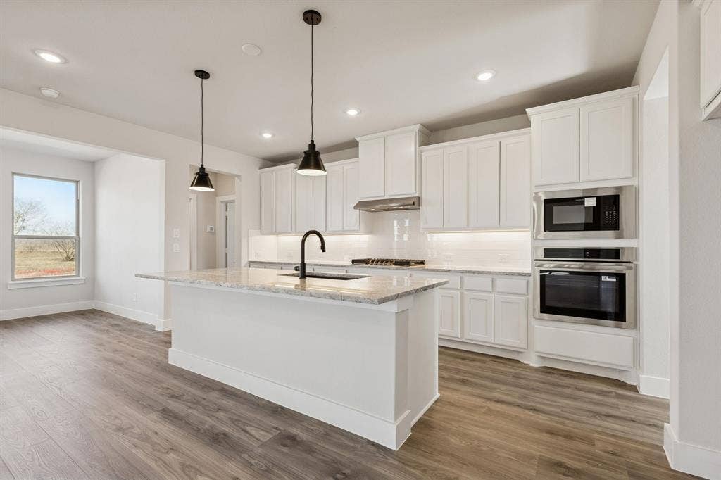 410 Rancher Trail, Waxahachie, TX 75165 Kitchen featuring an island with stone countertop, white cabinetry, integrated stainless steel appliances, and wood-finish flooring