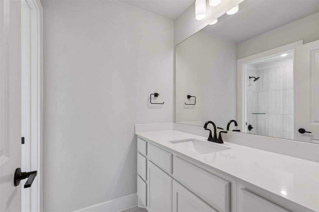 410 Rancher Trail, Waxahachie, TX 75165 White vanity with integrated sink, white countertop, matte black hardware, and wall-mounted mirror