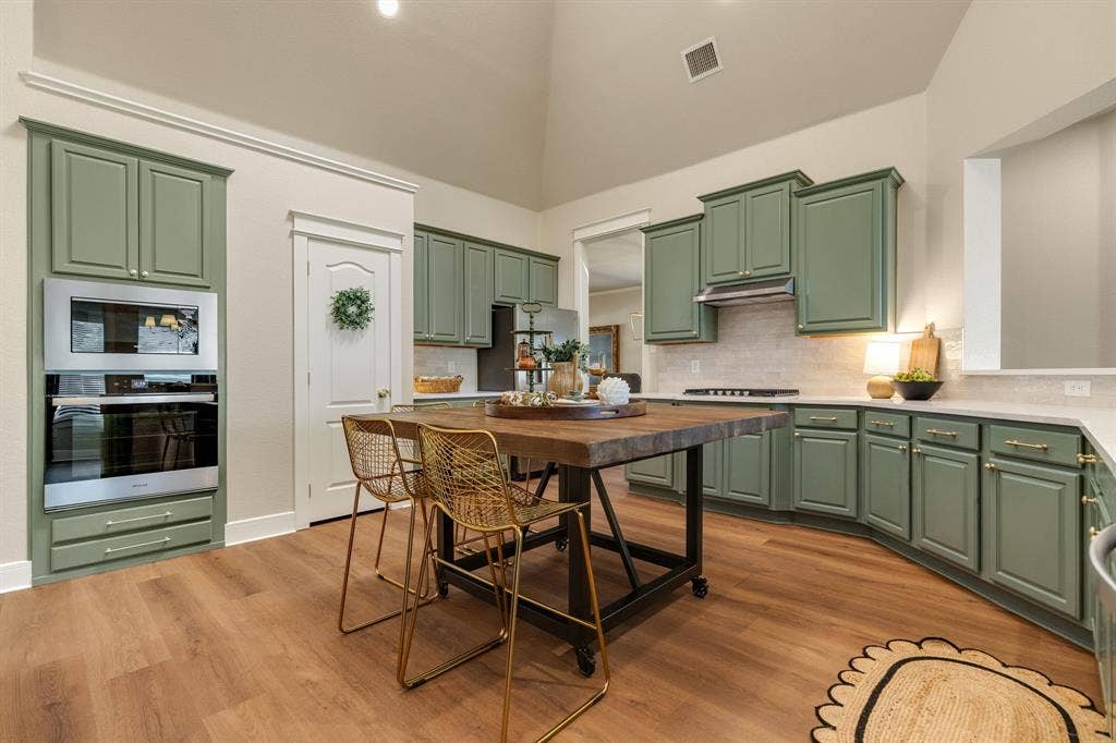 630 Candlewood Trail, Murphy, TX 75094 Vaulted ceiling kitchen featuring green cabinetry, stainless steel built-in appliances, light-toned countertops, tile backsplash, and wood-finish flooring