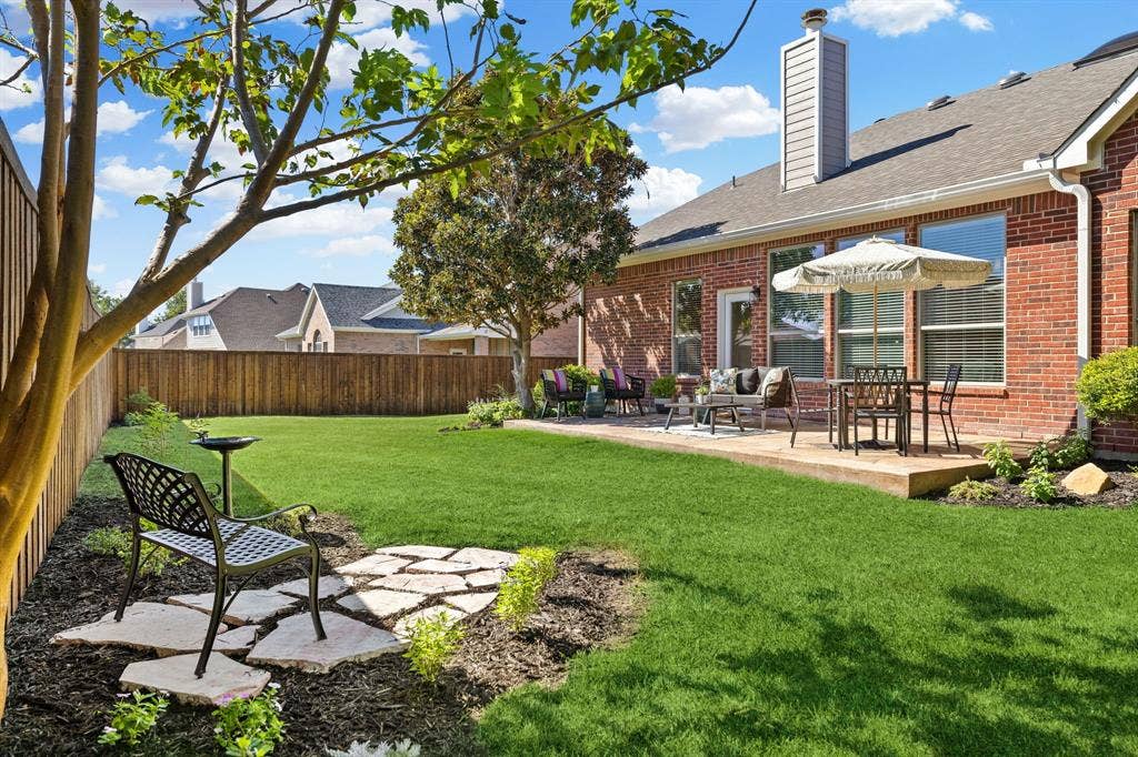 630 Candlewood Trail, Murphy, TX 75094 Expansive green lawn with a wood fence, concrete patio, and mature trees
