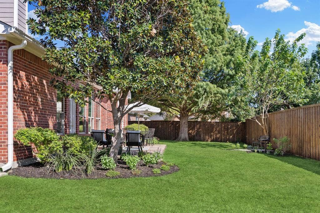 630 Candlewood Trail, Murphy, TX 75094 Brick exterior with large windows, mature trees, wood fence, and a patio area