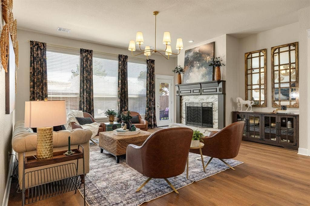 630 Candlewood Trail, Murphy, TX 75094 Living area with wood-finish flooring, a decorative fireplace with a marble-look surround and dark mantel, and multiple large windows