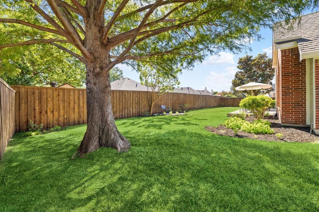 630 Candlewood Trail, Murphy, TX 75094 Expansive green lawn with a mature tree, solid wood fencing, and a brick exterior
