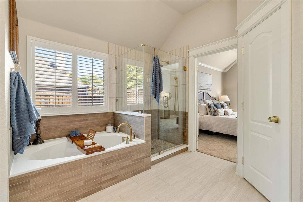 630 Candlewood Trail, Murphy, TX 75094 Soaking tub with brass-tone fixtures, wood-finish tile surround, and plantation shutters