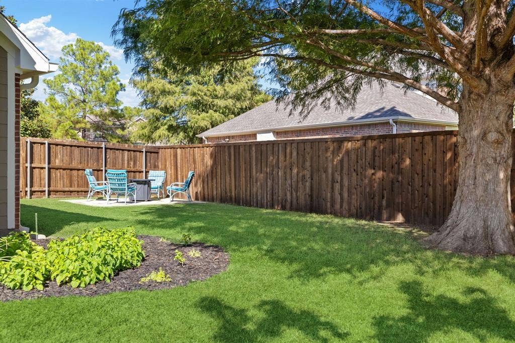 630 Candlewood Trail, Murphy, TX 75094 Expansive backyard featuring a manicured lawn, established shade tree, and wood privacy fencing