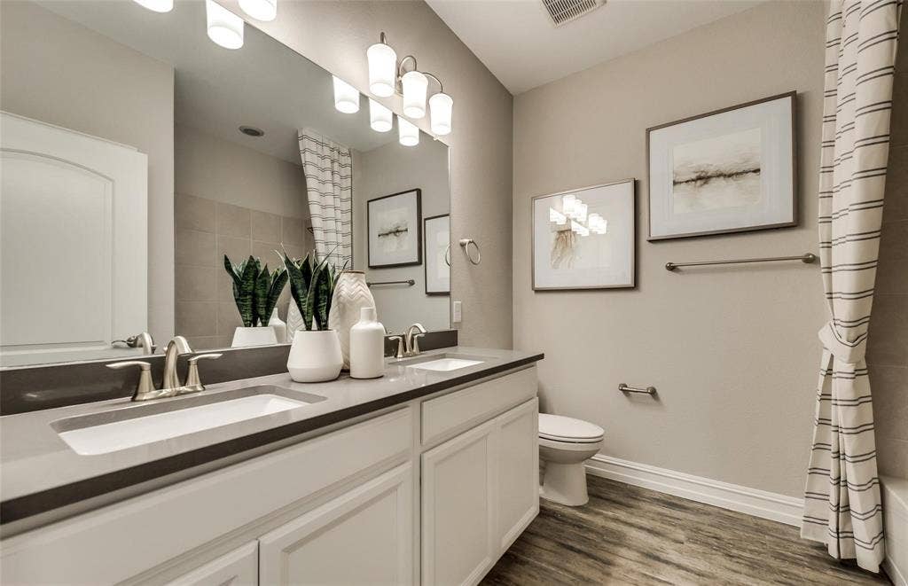 2816 southampton Drive, McKinney, TX 75071 Dual vanity with undermount sinks and dark countertops, wood-finish flooring, and a large wall mirror