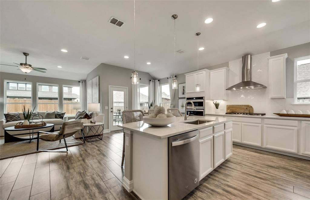 2816 southampton Drive, McKinney, TX 75071 Open-concept design featuring wood-finish flooring, a kitchen island with sink and integrated dishwasher, white shaker cabinetry, and a stainless steel range hood