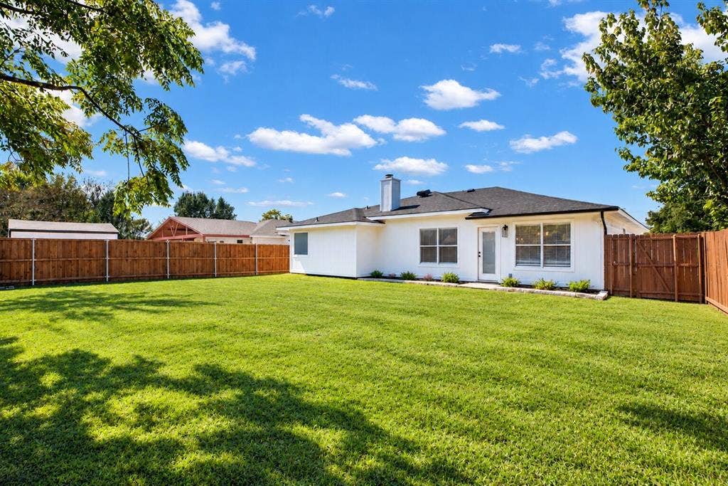 Expansive backyard with a manicured lawn, complete wood privacy fencing, and a crisp white exterior