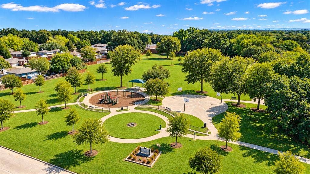 Green park space featuring a playground, basketball court, walking paths, and mature trees