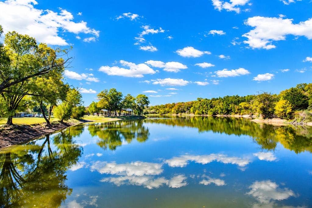 Waterfront property featuring a tranquil lake, mature trees, and a clear sky