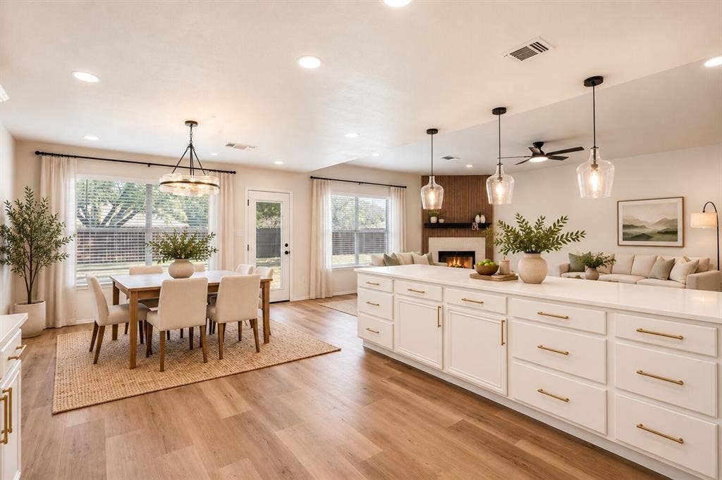 Expansive open-concept living space with wood-finish flooring, a large kitchen island with white cabinetry and gold-tone hardware, and recessed lighting