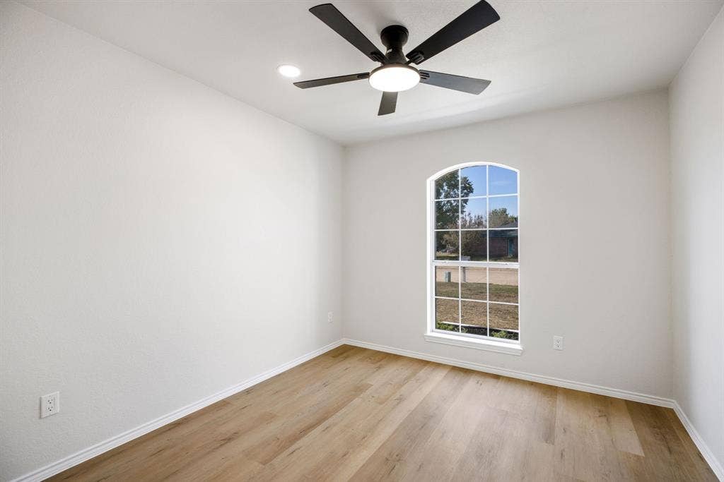 Arched window with white framing, wood-finish flooring, ceiling fan with integrated lighting, and white walls
