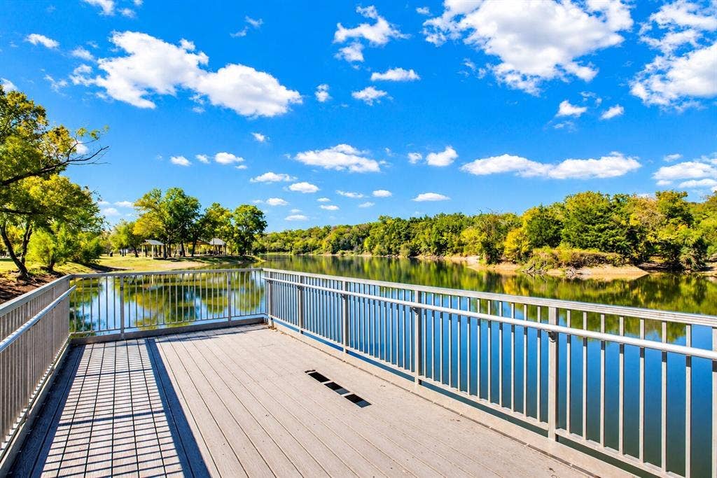 Expansive wooden deck with a metal railing overlooking a tranquil body of water, surrounded by lush green foliage and mature trees