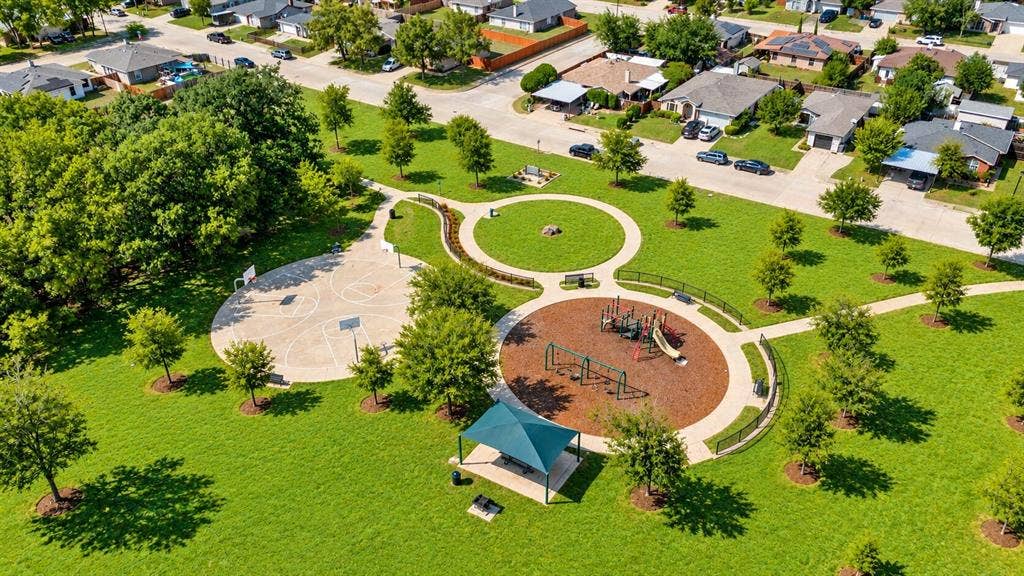 Expansive green space featuring walking paths, a dedicated playground area, basketball court, and mature trees