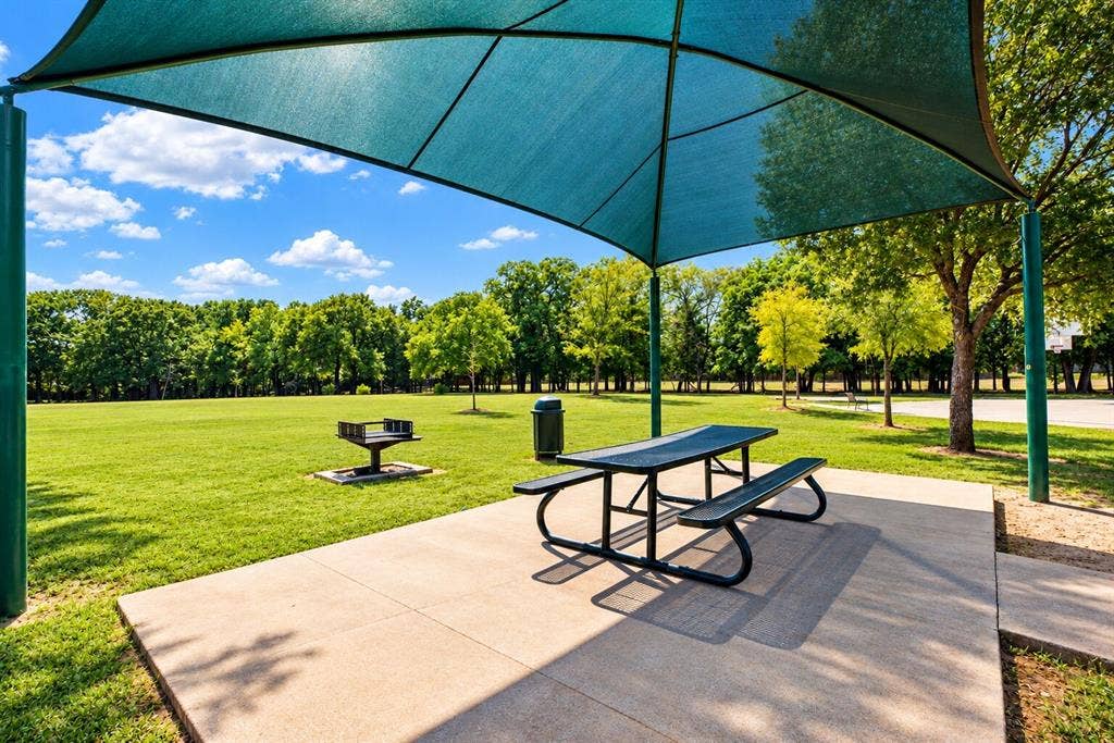 Covered picnic area with a concrete pad, metal picnic table, and expansive grassy field
