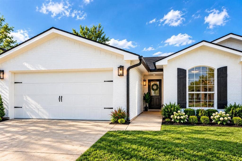 White brick exterior with black shutters, arched window with divided lites, attached garage, and a manicured lawn