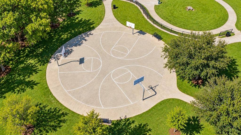 Concrete multi-court basketball area with three hoops, surrounded by green landscaping and walking paths