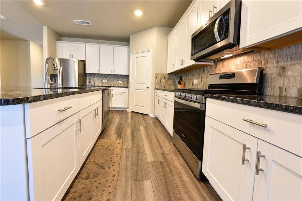 White shaker-style cabinetry, dark speckled countertops, stainless steel appliances, and wood-finish flooring