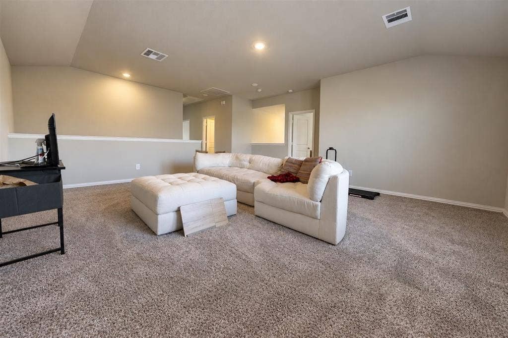 Spacious carpeted room featuring vaulted ceilings, recessed lighting, and a neutral color palette