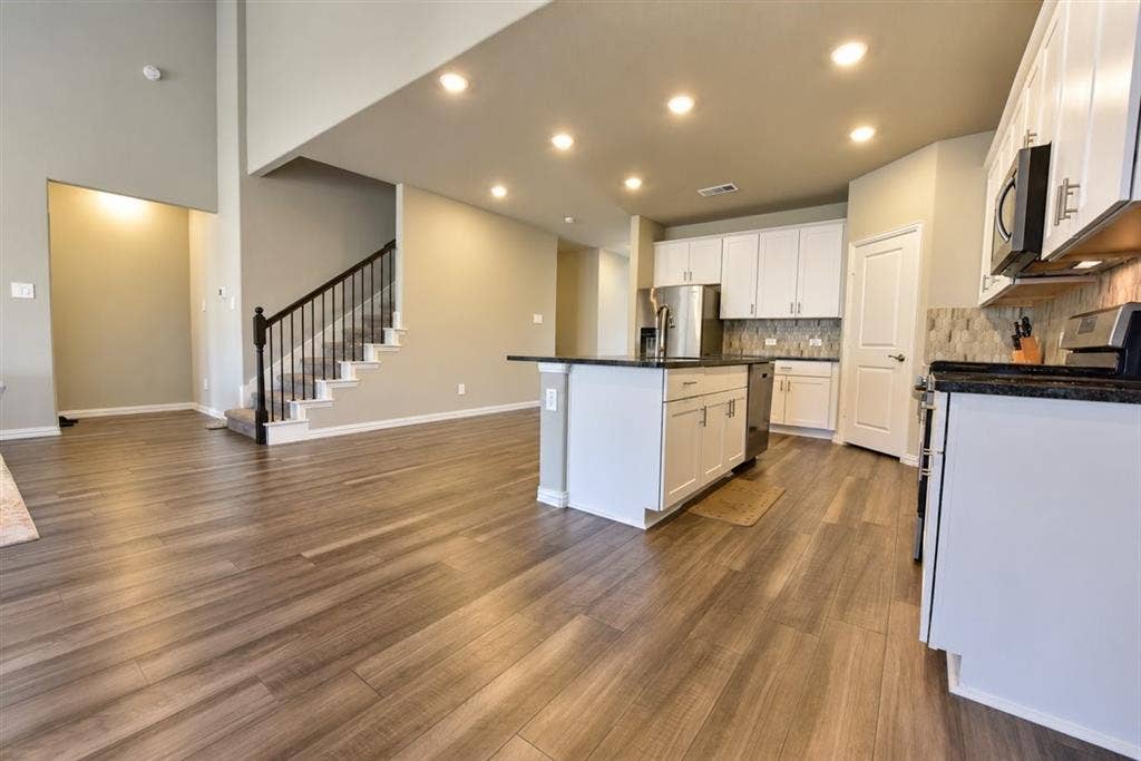 Open-concept living area with wood-finish flooring, recessed lighting, and a kitchen island with dark countertops
