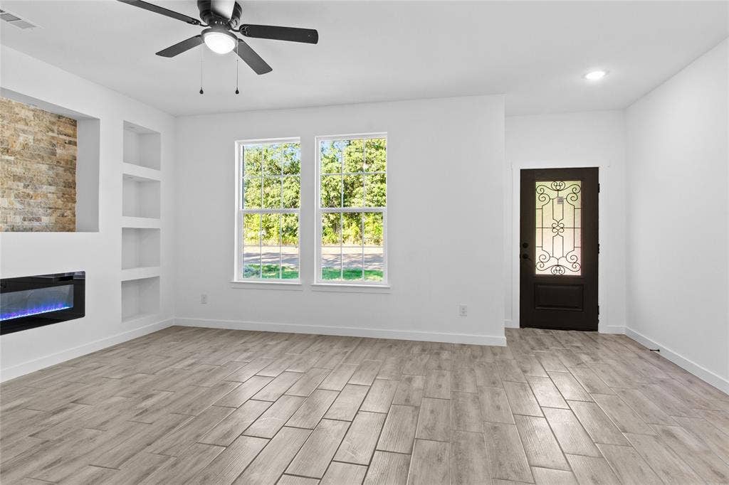 7520 Double Bridge Road, Mabank, TX 75156 Wood-finish tile flooring throughout, featuring a built-in fireplace with stone-finish accent, multiple recessed shelving niches, a ceiling fan, and a decorative front entry door