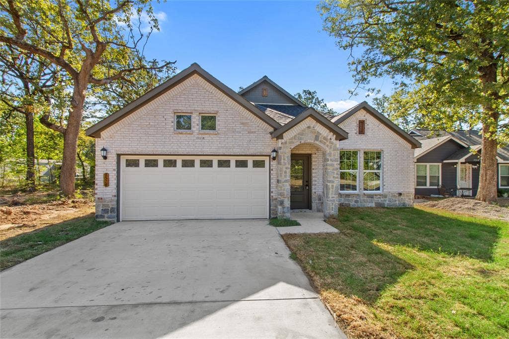 7520 Double Bridge Road, Mabank, TX 75156 Contemporary home featuring a light-colored brick exterior, stone archway entry, dark framed windows, a two-car garage, and a concrete driveway