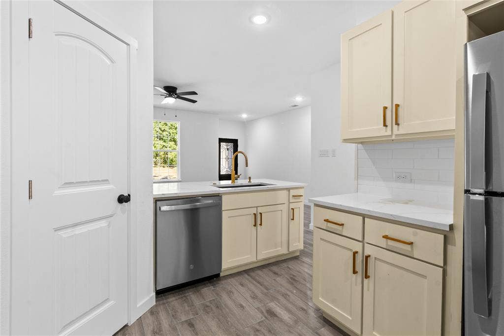 7520 Double Bridge Road, Mabank, TX 75156 Modern kitchen featuring cream-colored cabinetry with brushed brass hardware, stainless steel appliances including a dishwasher and refrigerator, white subway tile backsplash, wood-finish flooring, recessed ceiling lighting, and a ceiling fan