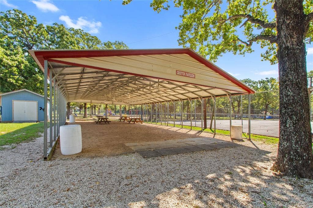 7520 Double Bridge Road, Mabank, TX 75156 Expansive covered pavilion with red metal roof and open-sided design, providing ample shade over gravel grounds