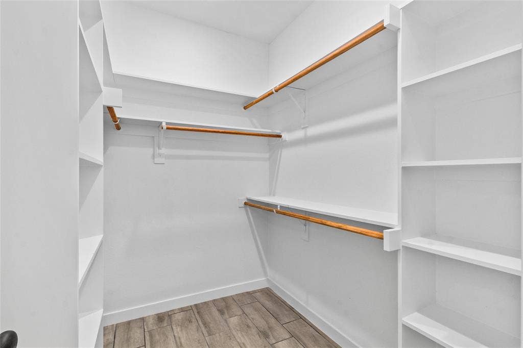 7520 Double Bridge Road, Mabank, TX 75156 Spacious walk-in closet featuring custom wood-finish hanging rods, white built-in shelving throughout, and wood-finish flooring