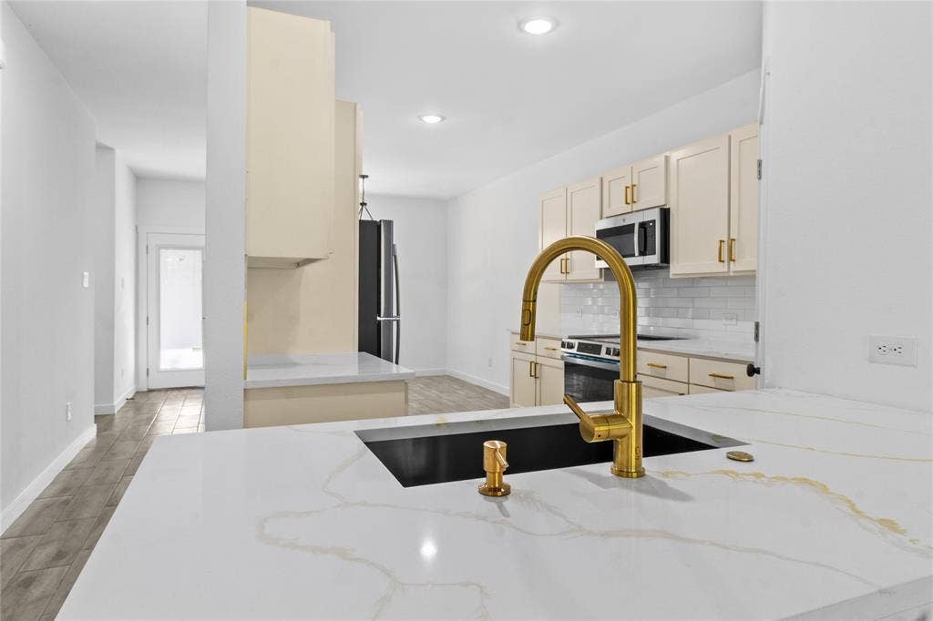 7520 Double Bridge Road, Mabank, TX 75156 Expansive kitchen island with a dark undermount sink and gold-tone faucet, complemented by light-toned cabinetry and a white subway tile backsplash, and recessed lighting