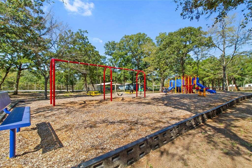 7520 Double Bridge Road, Mabank, TX 75156 Playground featuring a swing set, slides, and recreational structures over wood chip surfacing, bordered by a concrete retaining wall
