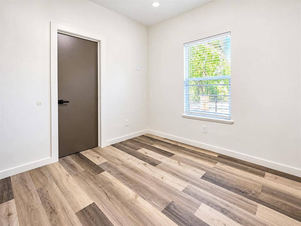 521 York Street, Athens, TX 75751 Wood-finish flooring, recessed ceiling lighting, a window with blinds, a modern door with dark hardware, and white wall finishes