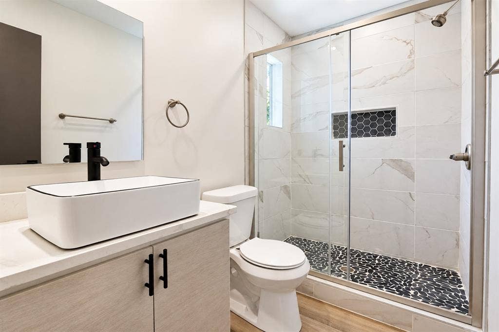 521 York Street, Athens, TX 75751 White vessel sink with a matte black faucet, vanity with light wood-finish cabinetry, and a walk-in shower featuring a glass enclosure
