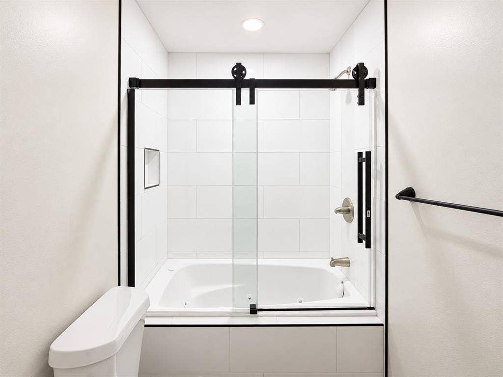 521 York Street, Athens, TX 75751 White tile surround bathtub with black framed sliding glass door, brushed nickel fixtures, and recessed shelf
