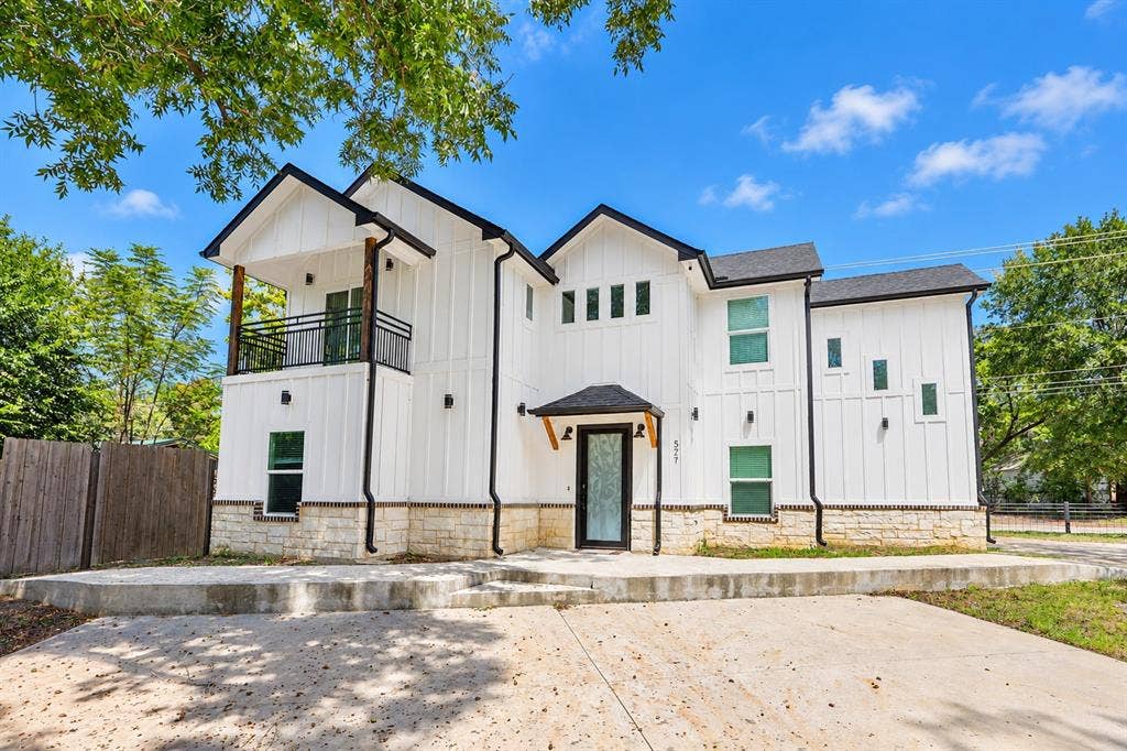 521 York Street, Athens, TX 75751 Modern architectural design featuring white board and batten siding, stone facade accents, a black shingle roof, and a second-story balcony with metal railings