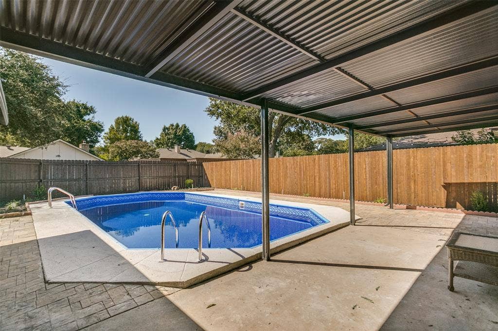 2704 Parkhaven Drive, Plano, TX 75075 Covered patio area featuring a swimming pool with concrete decking, a corrugated metal roof, and a wood privacy fence