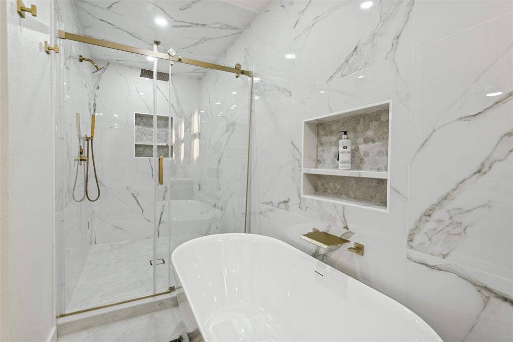 2704 Parkhaven Drive, Plano, TX 75075 Freestanding soaking tub, large format wall tiling, glass-enclosed shower with gold-tone fixtures, and recessed shelving