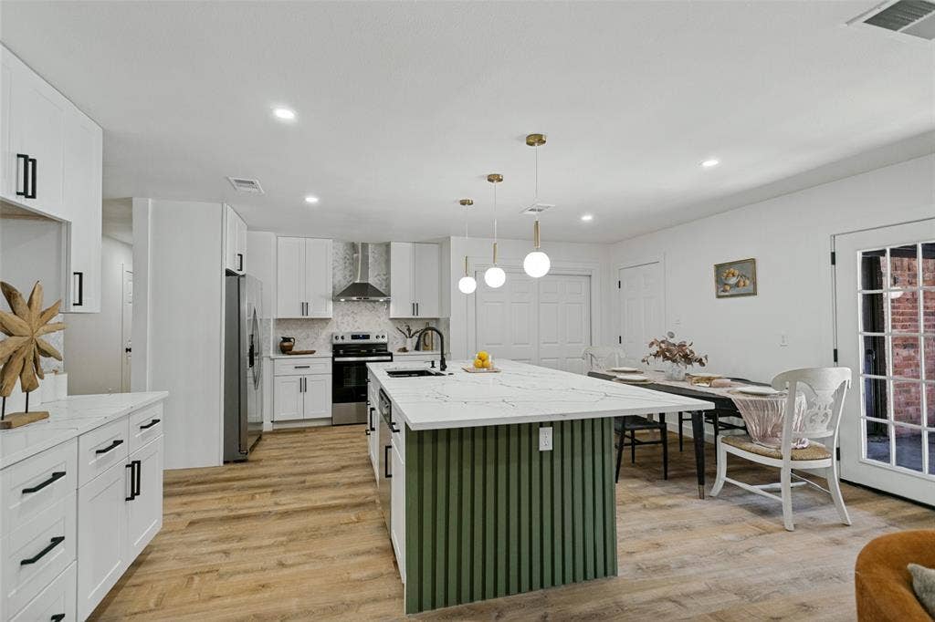 2704 Parkhaven Drive, Plano, TX 75075 Kitchen featuring wood-finish flooring, white cabinetry with black hardware, stainless steel appliances, and a central island with a white countertop